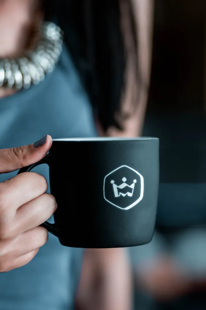 Programvaruutvecklare håller i en svart Ministry of Programming-kaffemugg med företagets logotyp under en paus på kontoret.